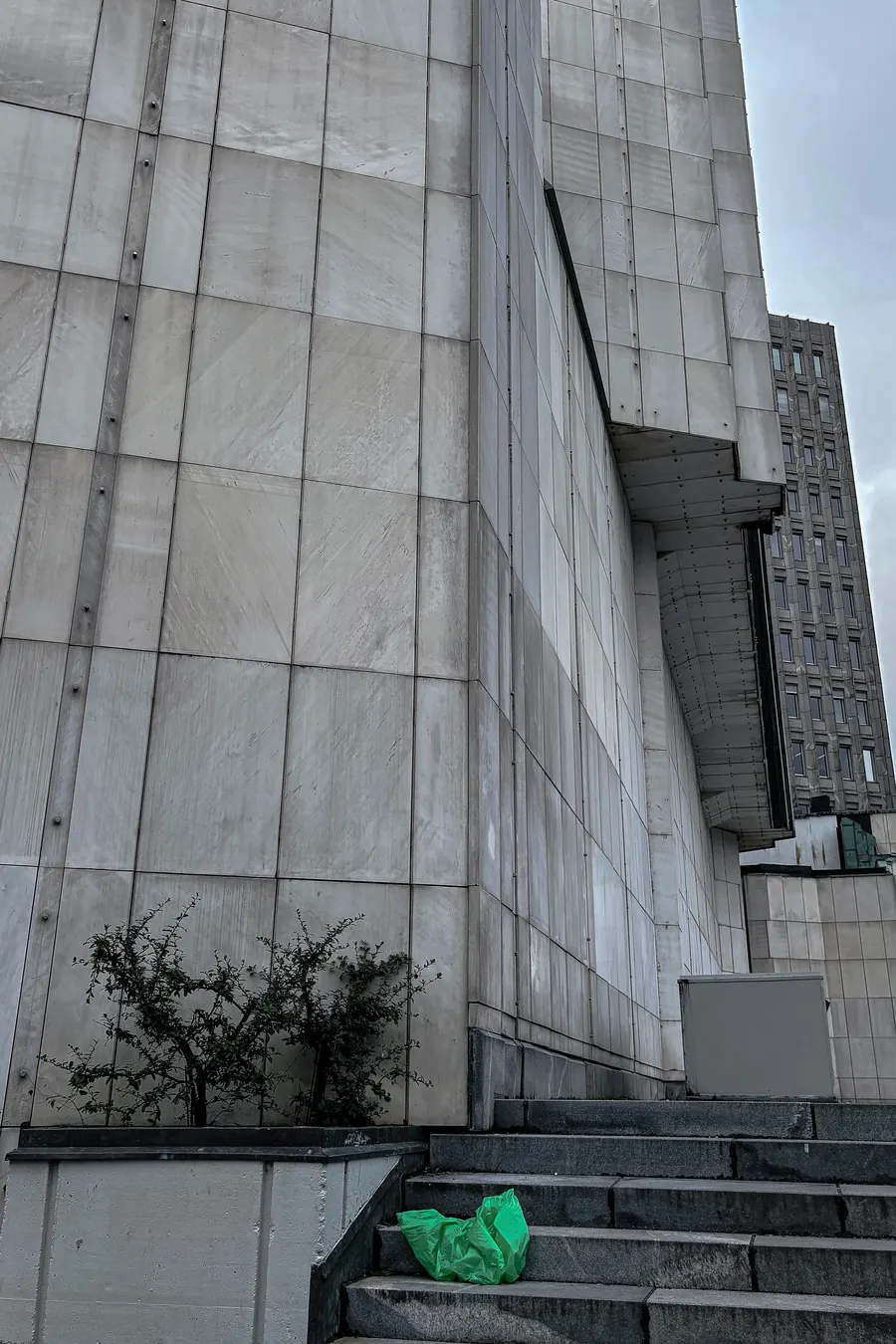 Massive stone-clad wall above steps, a green plastic bag at its foot