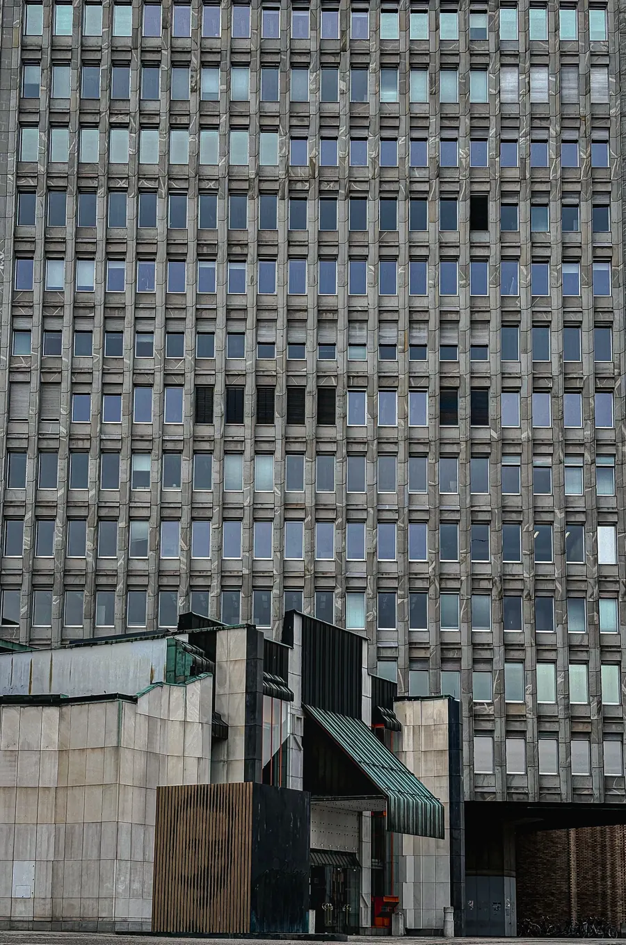 Gridded office tower above a low pavilion with a green canopy