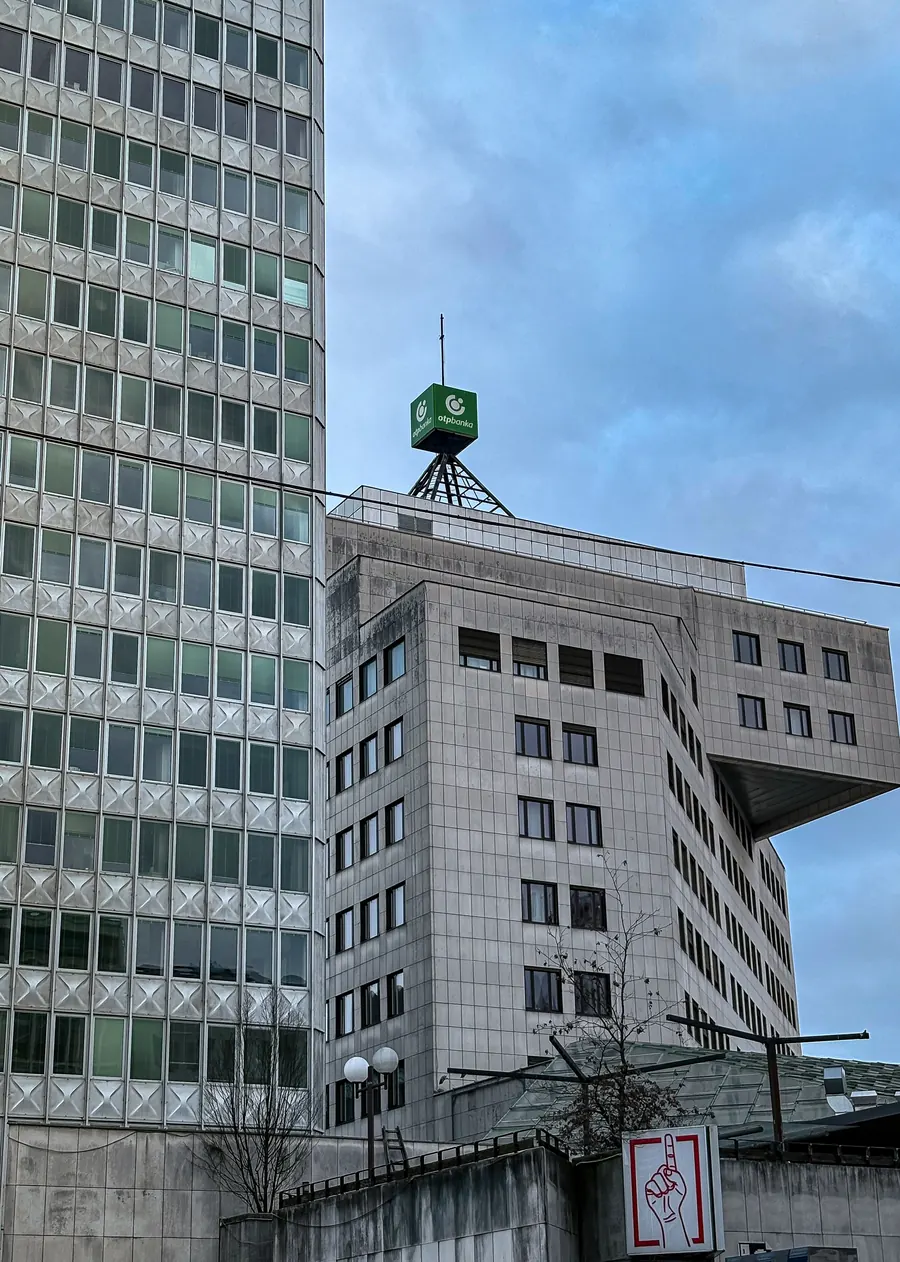 Gridded tower beside a cantilevered block crowned by a green cube