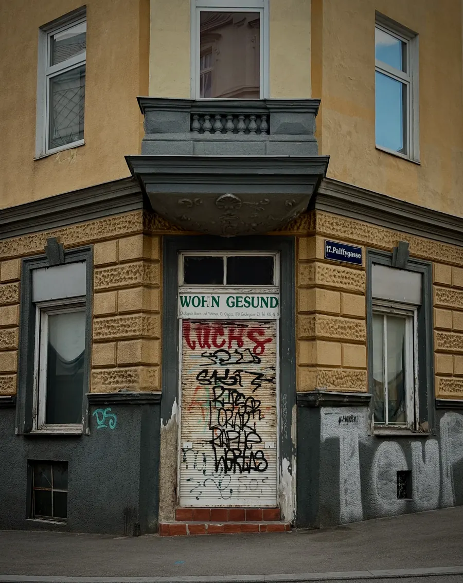 Corner entrance covered in graffiti beneath an old sign reading Woh'n gesund, Vienna