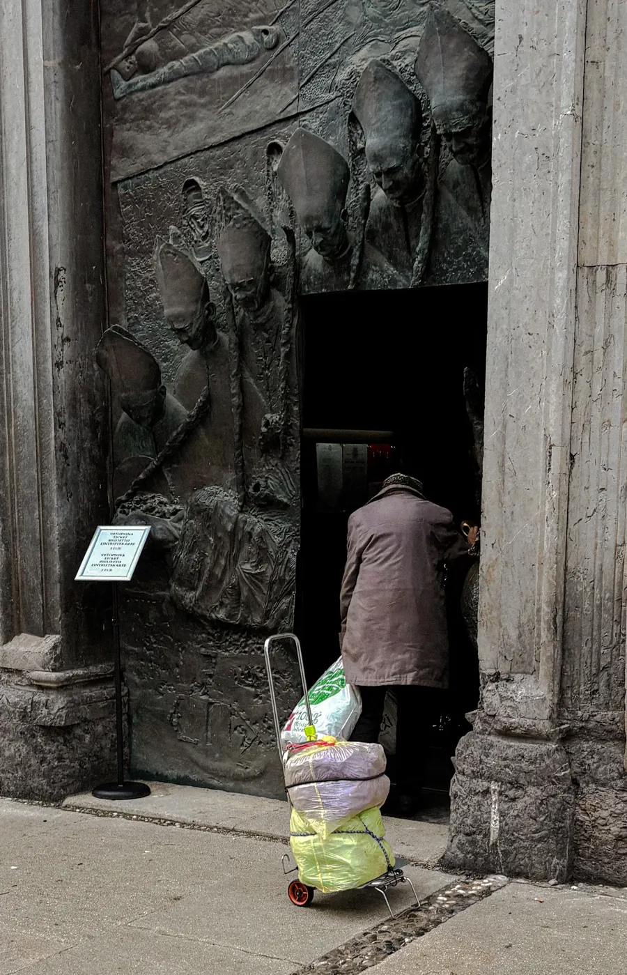 Woman with a shopping trolley entering a bronze church door