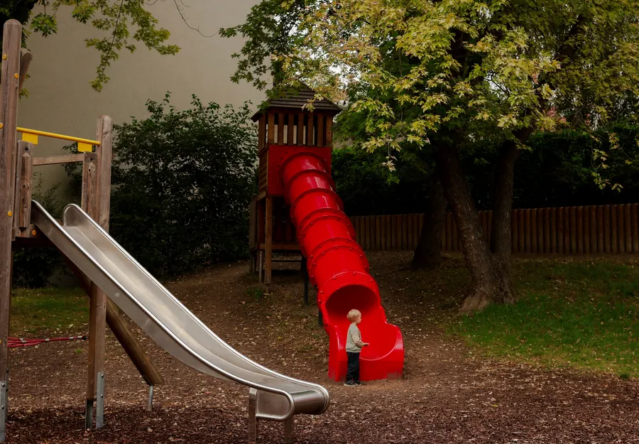Child at the foot of a red tube slide in a park playground