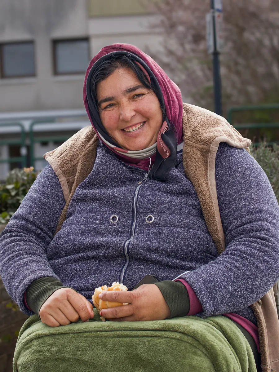 Smiling woman in a headscarf, seated, holding a pastry