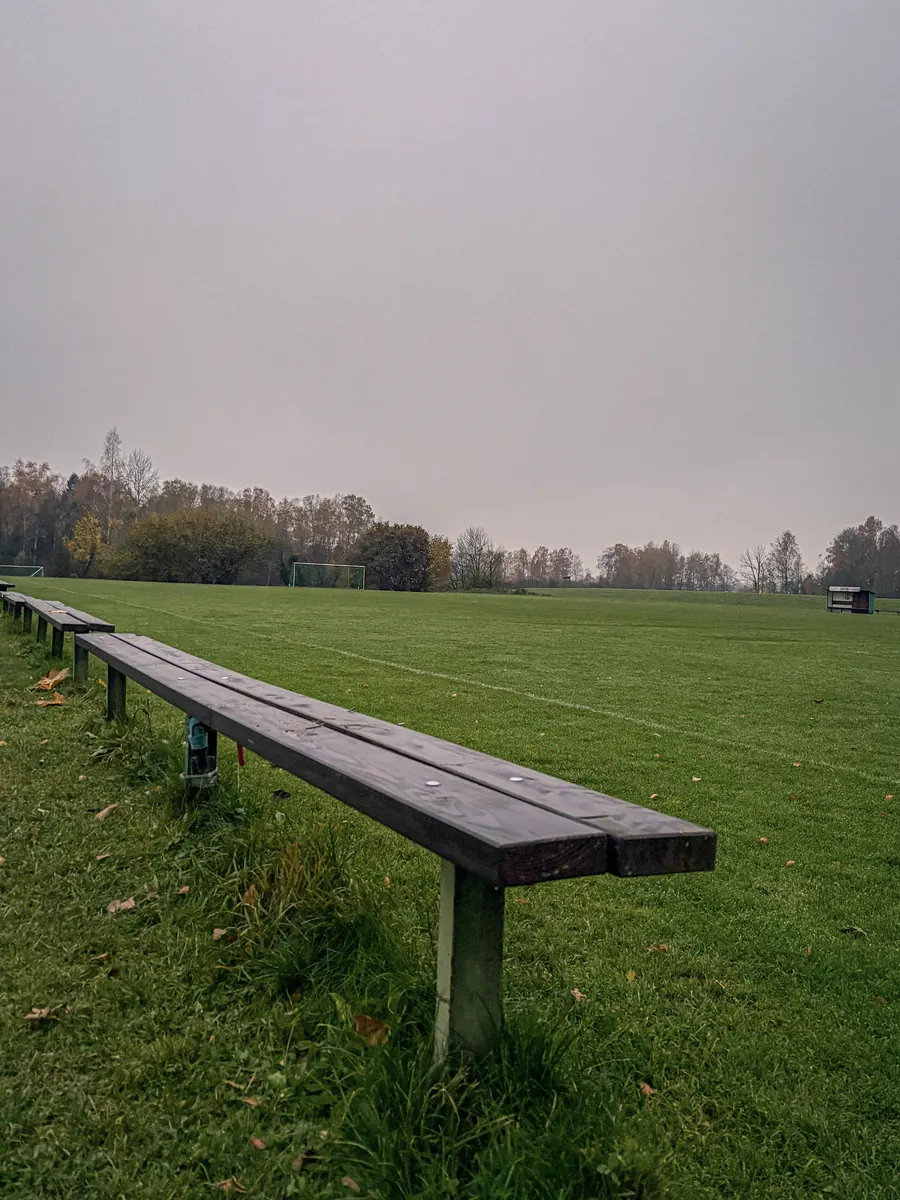 Long empty bench along a sports field under a grey sky
