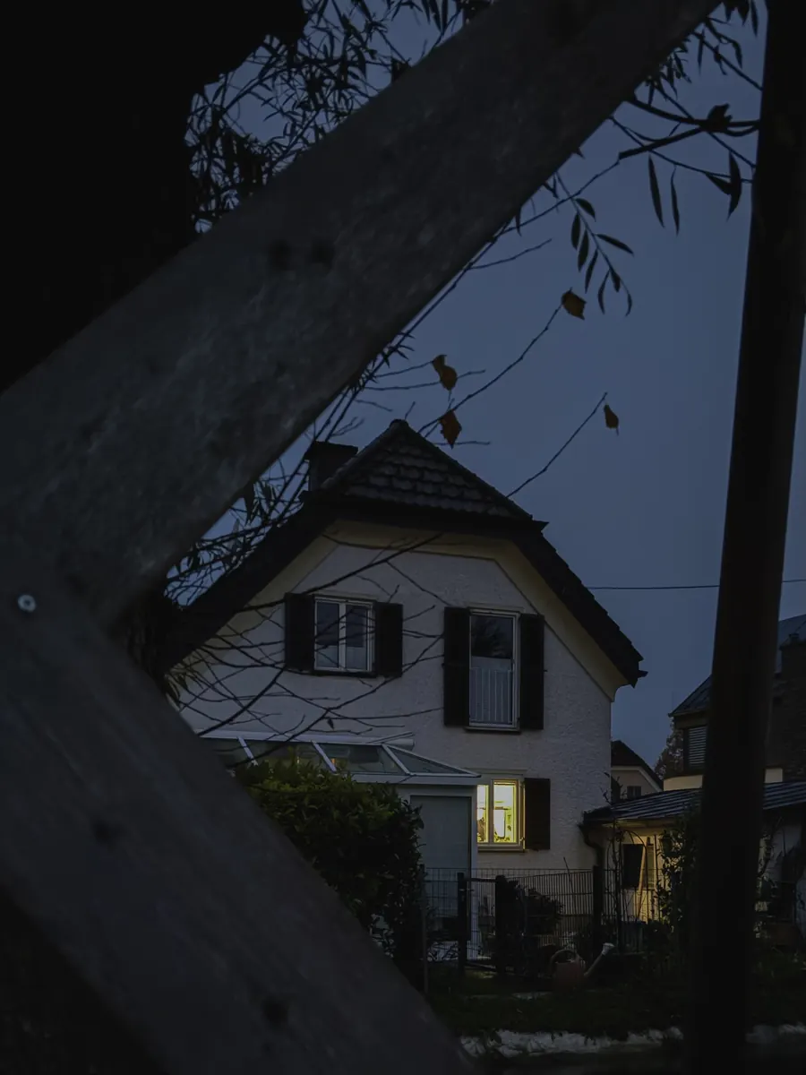 House with one lit window framed by leaning timber beams at dusk