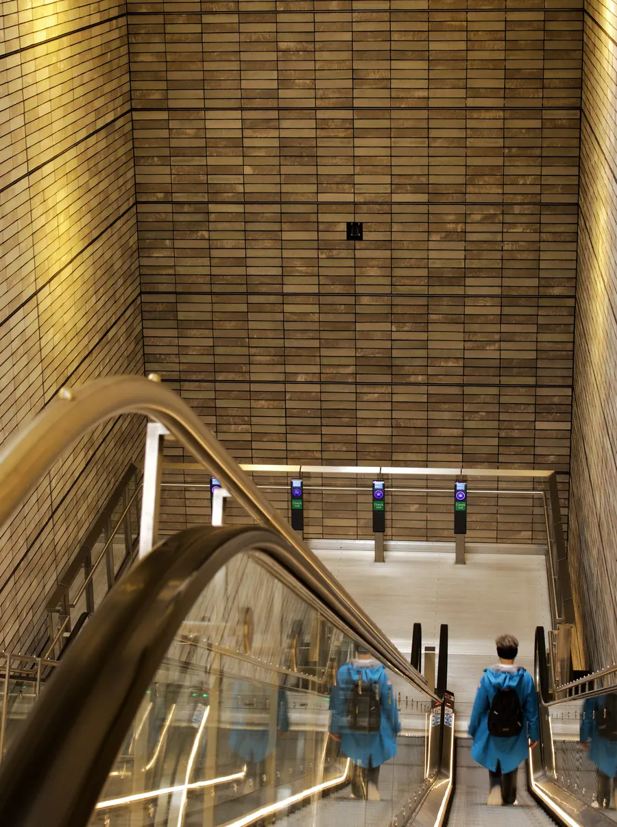 Looking down a long escalator, passengers in blue raincoats